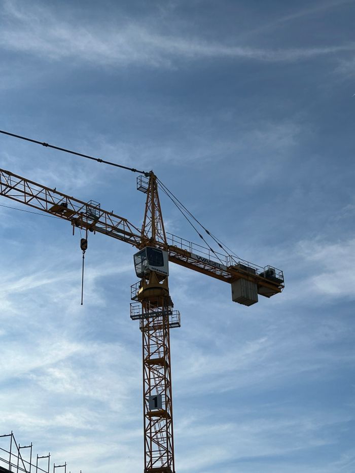 Tall tower crane at a construction site with a clear blue sky background, showcasing construction industry machinery.